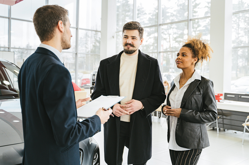 A car salesman talking to a couple at an auto dealership